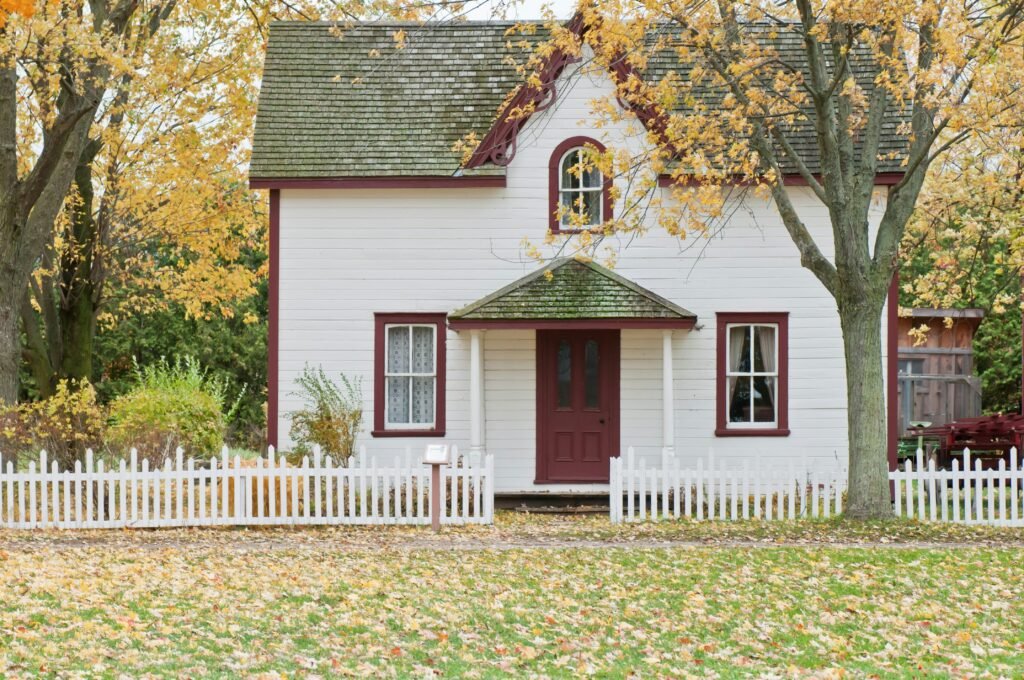 Charming House with a white picket fence surrounded by trees and autumn foilage, creating a cozy and inviting home atmostphere.